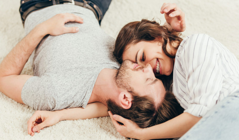 Ein Paar liegt entspannt auf dem Boden und lächelt sich an, was die enge Verbindung zwischen Darm und Psyche symbolisiert. Diese Beziehung wird oft durch die Bedeutung der Darmflora in der emotionalen Gesundheit hervorgehoben.