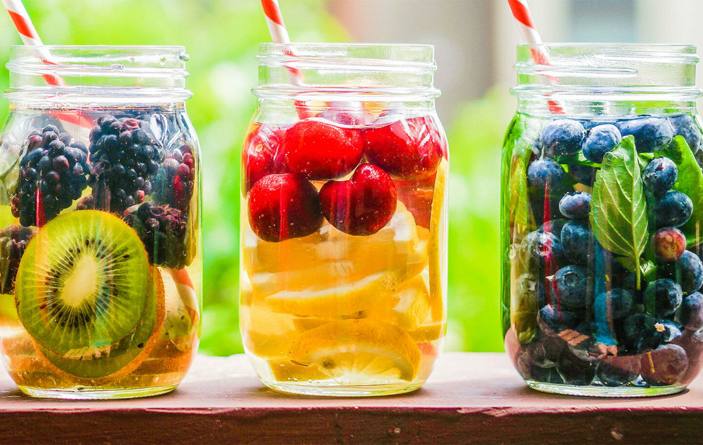 Glasgefäße mit frischen Früchten wie Kiwi, Brombeeren, Kirschen und Blaubeeren, die in Wasser eingelegt sind, zur Unterstützung einer Entschlackungskur.