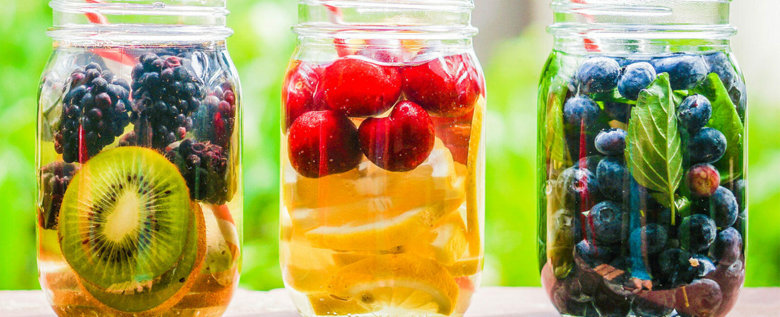 Glasgefäße mit frischen Früchten wie Kiwi, Brombeeren, Kirschen und Blaubeeren, die in Wasser eingelegt sind, zur Unterstützung einer Entschlackungskur.