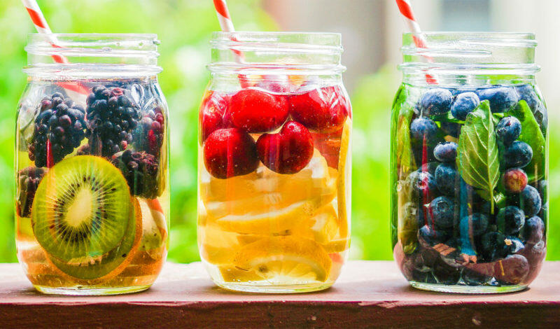 Glasgefäße mit frischen Früchten wie Kiwi, Brombeeren, Kirschen und Blaubeeren, die in Wasser eingelegt sind, zur Unterstützung einer Entschlackungskur.
