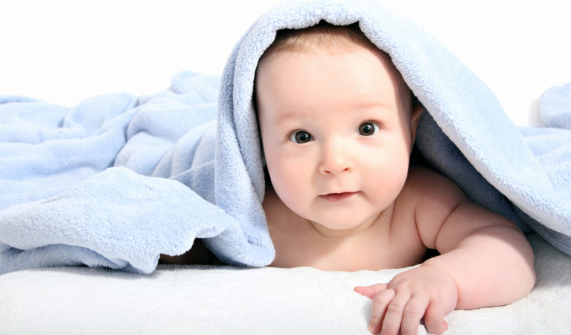 Neugeborenes Baby mit blauer Decke, das neugierig in die Kamera schaut. Tipps zur Stärkung des Immunsystems bei Neugeborenen werden in diesem Artikel behandelt.