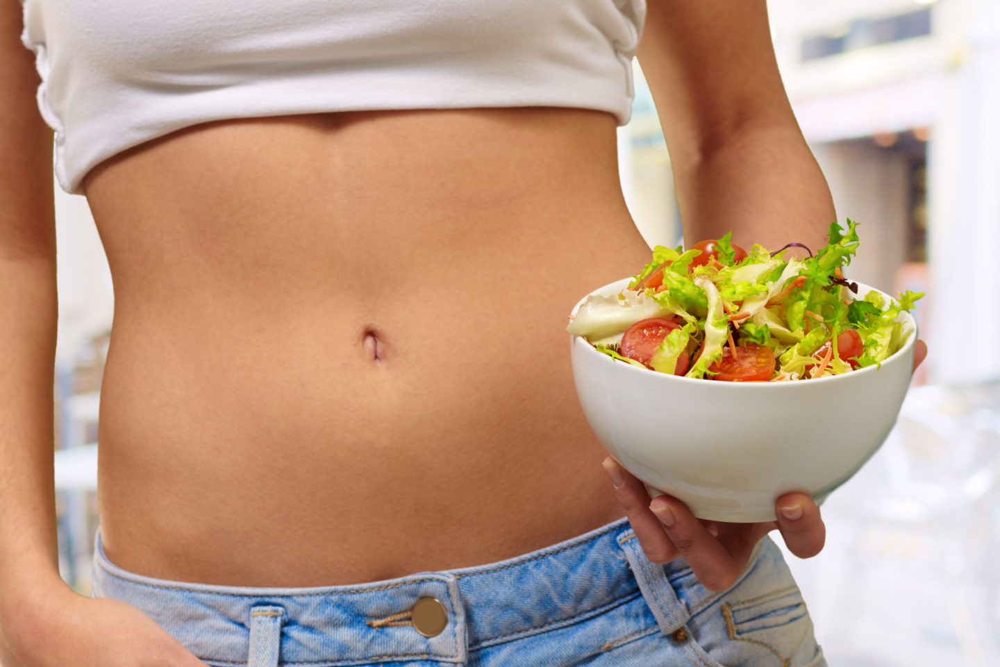 Frau hält eine Schüssel mit frischem Salat vor ihrem Bauch, symbolisiert gesunde Ernährung für die Darmflora.