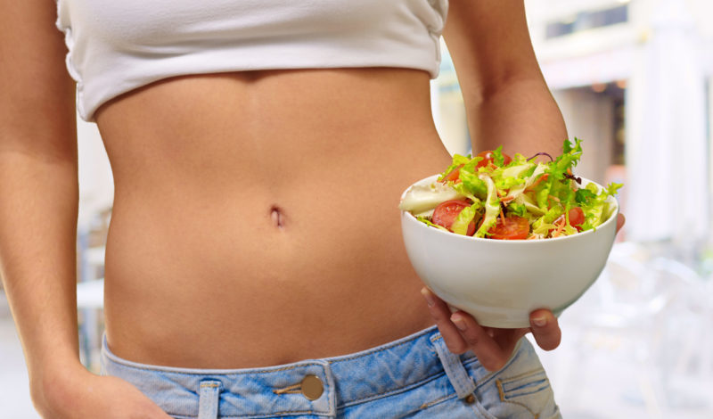 Frau hält eine Schüssel mit frischem Salat vor ihrem Bauch, symbolisiert gesunde Ernährung für die Darmflora.