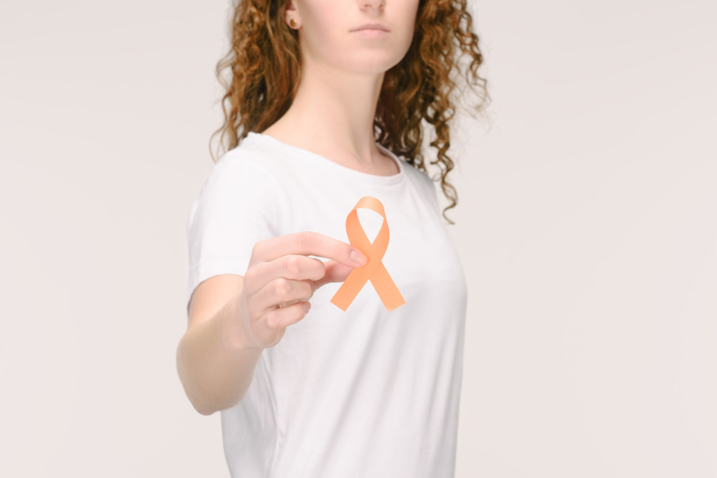 Junge Frau in einem weißen T-Shirt hält ein orangefarbenes Bewusstseinsband in der Hand, symbolisiert Unterstützung für Multiple Sklerose.