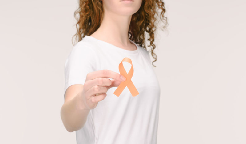 Junge Frau in einem weißen T-Shirt hält ein orangefarbenes Bewusstseinsband in der Hand, symbolisiert Unterstützung für Multiple Sklerose.