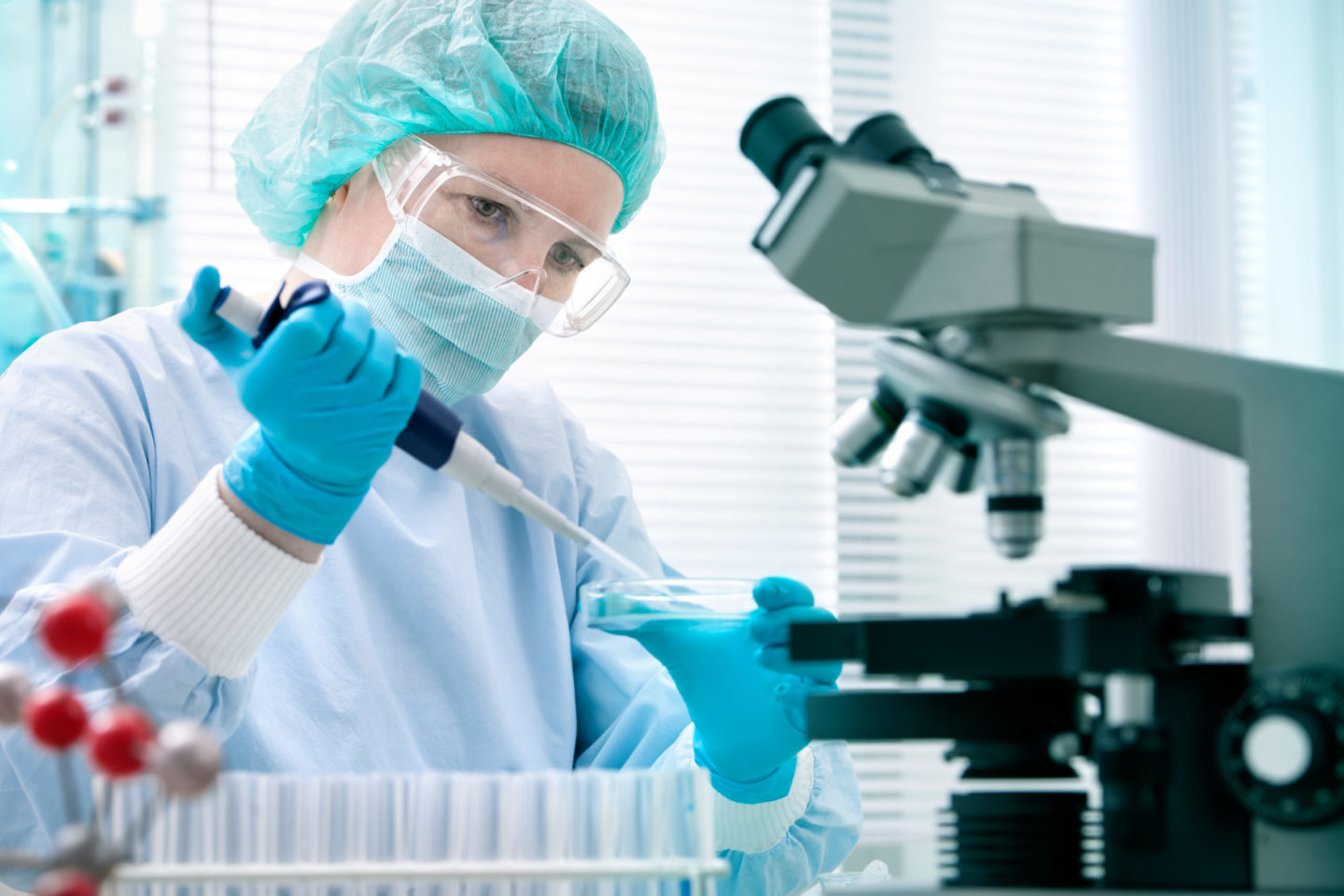 Wissenschaftlerin im Labor, die mit einer Pipette Proben in eine Petrischale überträgt, während ein Mikroskop im Hintergrund steht. Fokus auf DNA-Tests und Darmflora-Forschung.