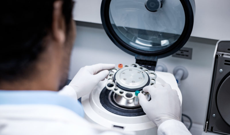 Wissenschaftler in einem Labor bedient eine Zentrifuge, um Proben effizient zu trennen. Die Person trägt Handschuhe und konzentriert sich auf den Prozess, während die Zentrifuge bereit ist, in Betrieb genommen zu werden.