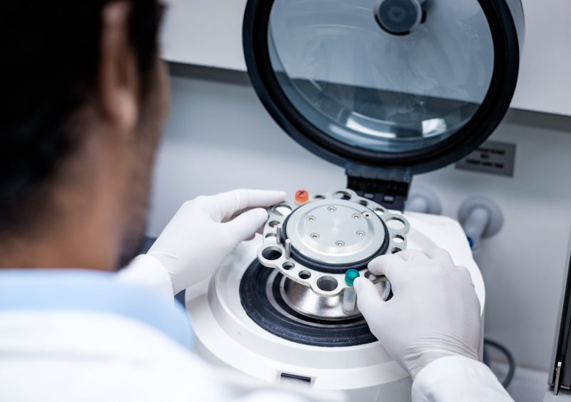 Wissenschaftler in einem Labor bedient eine Zentrifuge, um Proben effizient zu trennen. Die Person trägt Handschuhe und konzentriert sich auf den Prozess, während die Zentrifuge bereit ist, in Betrieb genommen zu werden.
