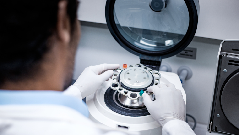 Wissenschaftler in einem Labor bedient eine Zentrifuge, um Proben effizient zu trennen. Die Person trägt Handschuhe und konzentriert sich auf den Prozess, während die Zentrifuge bereit ist, in Betrieb genommen zu werden.