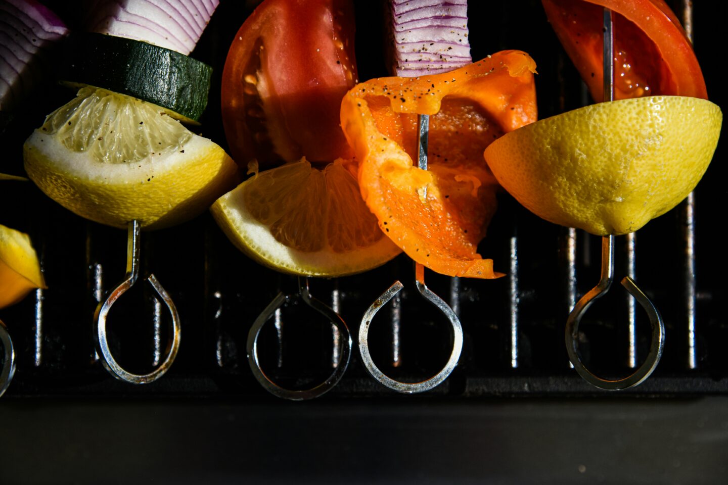Bunte Gemüsespieße mit Paprika, Zucchini, Zwiebeln und Zitronenscheiben auf einem Grillrost, bereit zum Grillen.