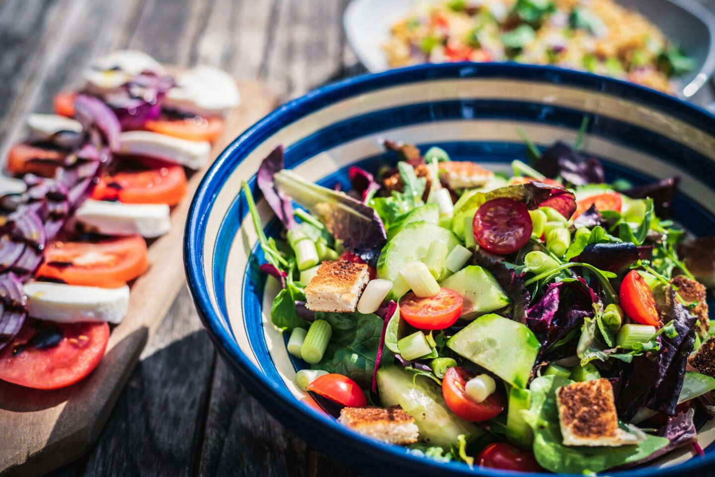Bunte Salatschüssel mit frischem Gemüse, darunter Gurken, Tomaten und Blattsalate, serviert auf einem rustikalen Holztisch.