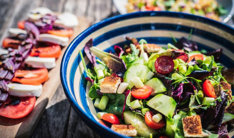 Bunte Salatschüssel mit frischem Gemüse, darunter Gurken, Tomaten und Blattsalate, serviert auf einem rustikalen Holztisch.