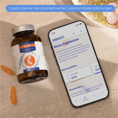 Nahrungs&shy;ergänzungs&shy;mittel-Flasche neben einem Smartphone, das Ergebnisse benutzerdefinierter Empfehlungen anzeigt, auf einem hellen Tisch mit gesunden Lebensmitteln im Hintergrund.