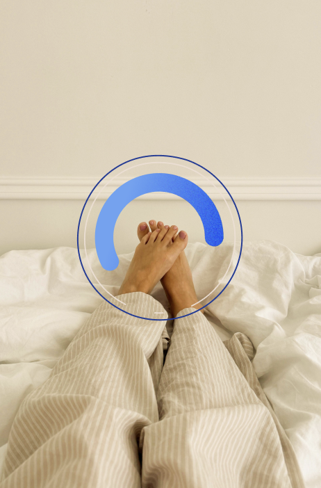 Füße einer Person, die entspannt auf einem Bett liegen, umgeben von einer hellen, gemütlichen Bettwäsche. Ein blauer, runder Umriss betont die Füße, was auf Entspannung und Wohlbefinden hinweist.