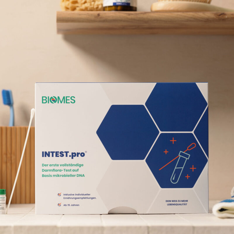 Produktverpackung von INTTEST.pro auf einer Arbeitsfläche, umgeben von Zahnbürsten und anderen Hygieneartikeln, zeigt eine moderne und ansprechende Gestaltung für einen Darmgesundheitstest.