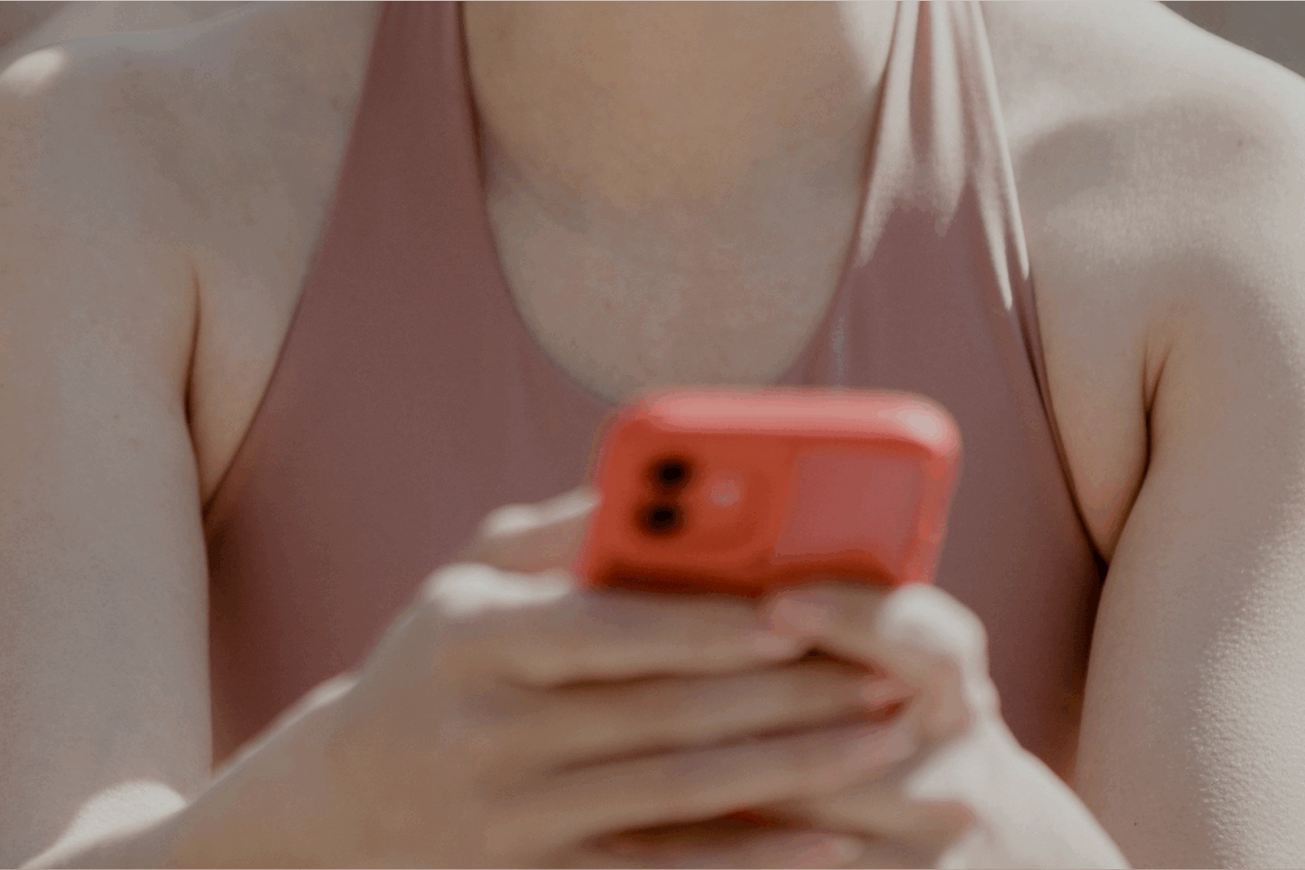 Junge Person in Sportkleidung hält ein rotes Smartphone in den Händen, während sie im Freien sitzt.