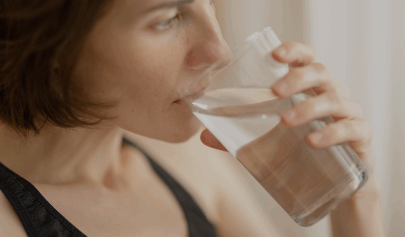 Eine Person trinkt aus einem Glas Wasser, während sie sich mit Themen rund um Probiotika und Fructoseintoleranz beschäftigt. Diese Darstellung verdeutlicht die Bedeutung von Flüssigkeitszufuhr bei der Ernährung mit Probiotika für Menschen mit Fructoseintoleranz.