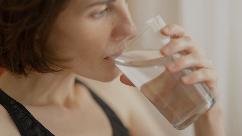 Eine Person trinkt aus einem Glas Wasser, während sie sich mit Themen rund um Probiotika und Fructoseintoleranz beschäftigt. Diese Darstellung verdeutlicht die Bedeutung von Flüssigkeitszufuhr bei der Ernährung mit Probiotika für Menschen mit Fructoseintoleranz.